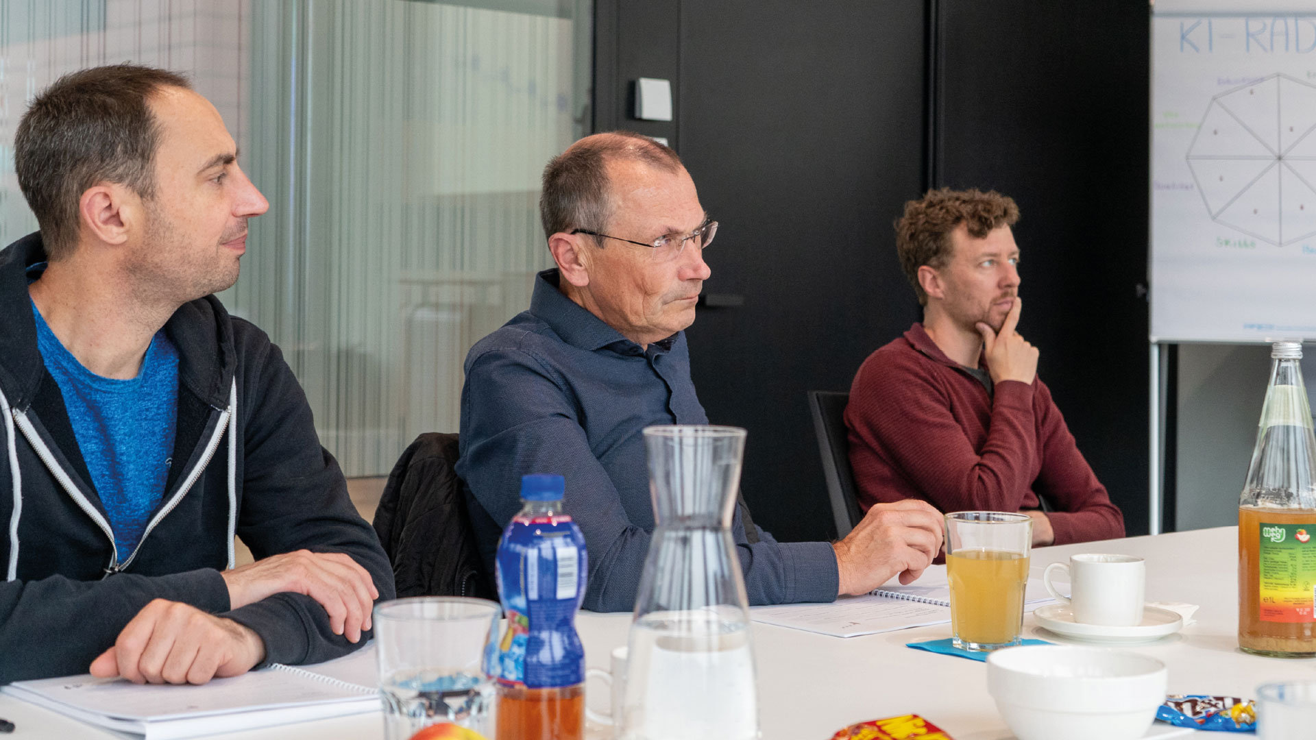 wbi-academy-zert-wm-teilnehmer-web Drei Männer sitzen an einem Tisch und hören aufmerksam zu.