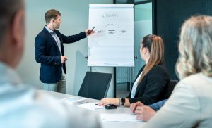 wbi-academy-zertifizierter-wm-kurs-web Alexander Cavada zeigt mehreren Personen eine Grafik auf einem Flip-Chart. Es handelt sich dabei um den bewährten WBI-Prozess, der dafür sorgt, dass Wissen verteilt, weiterentwickelt und laufend genutzt wird.