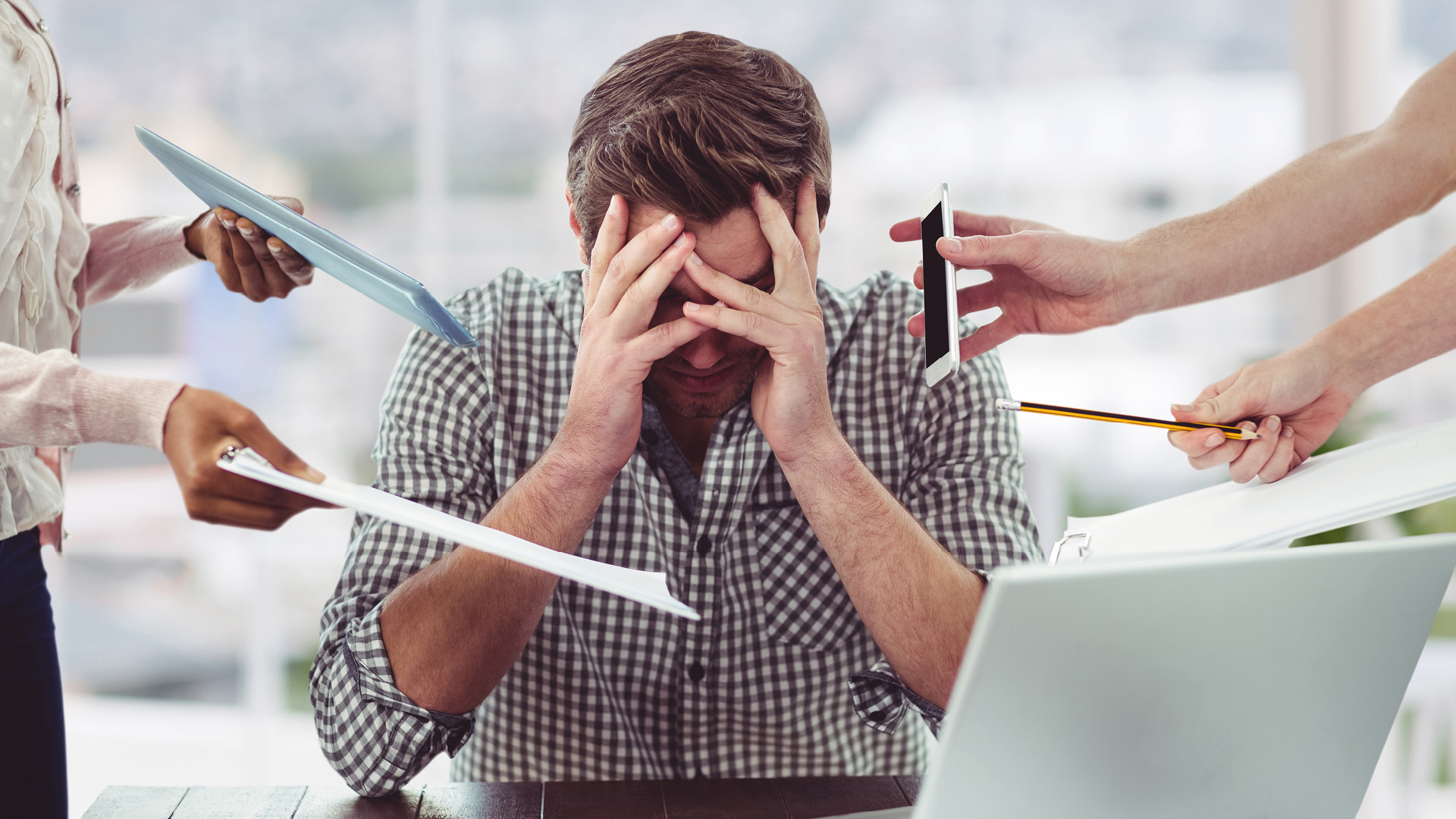 Ein gestresster Mann sitzt am Schreibtisch und hält sich den Kopf. Er ist umgeben von mehreren Personen, die ihm Unterlagen und ein Telefon hinstrecken. Wenn auch du oft gestresst bist im Arbeitsalltag, ist es Zeit für Wissensmanagement mit WIVIO von WBI.