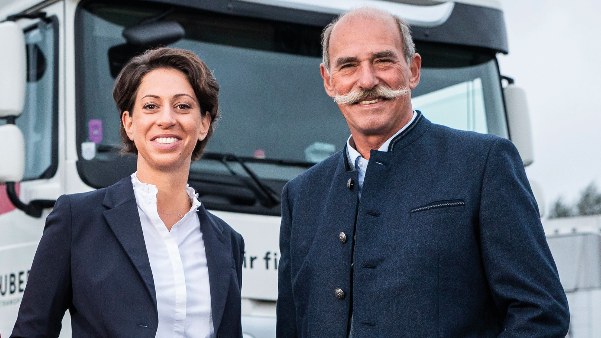 Sabrina Huber und ihr Vater posieren vor einem LKW der Huber Transporte GmbH & Co KG in Hard. Es handelt sich um das Titelbild zur Success Story von WBI und Huber Transporte, in der die Erfolgsgeschichte der Betriebsnachfolge beschrieben wird.