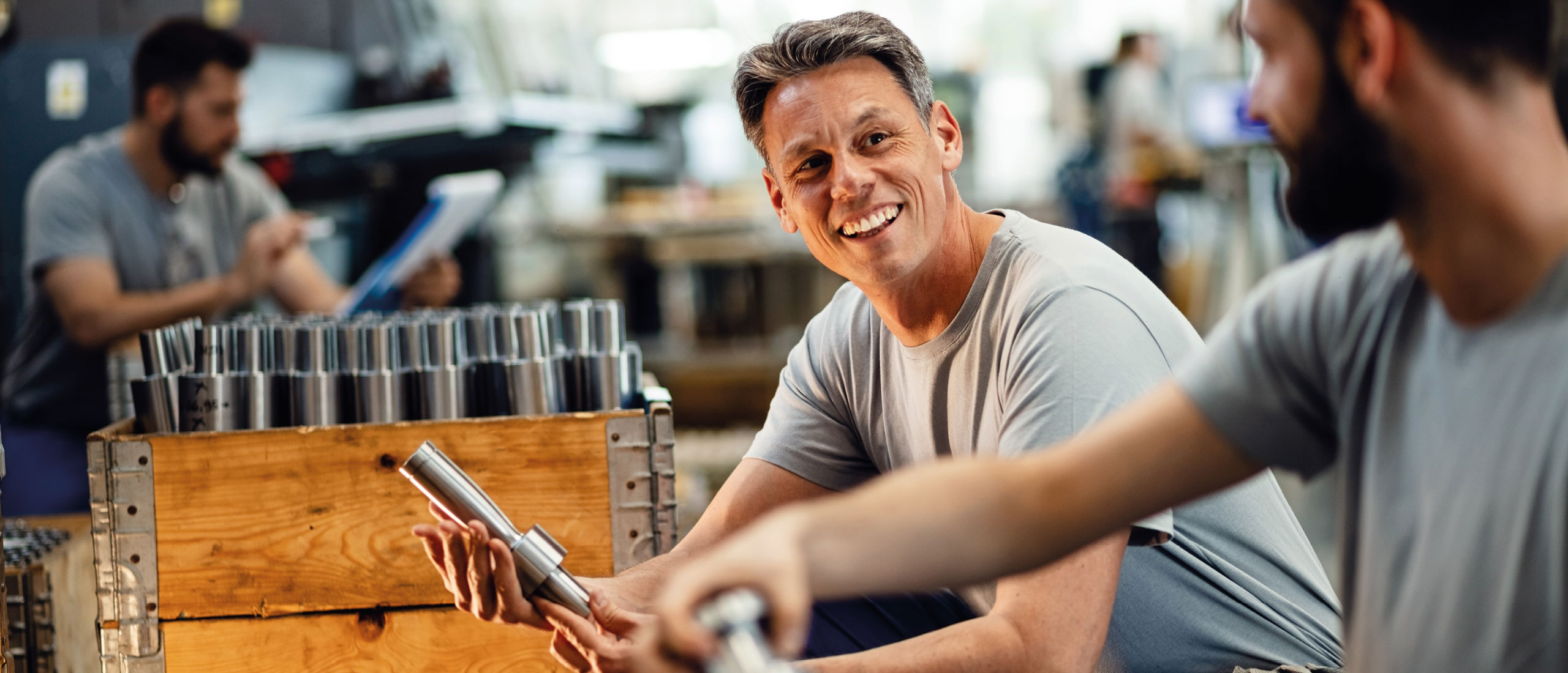 Arbeiter in einer Fabrik unterhalten sich während der Arbeit in der Produktion und hantieren mit Metallteilen.