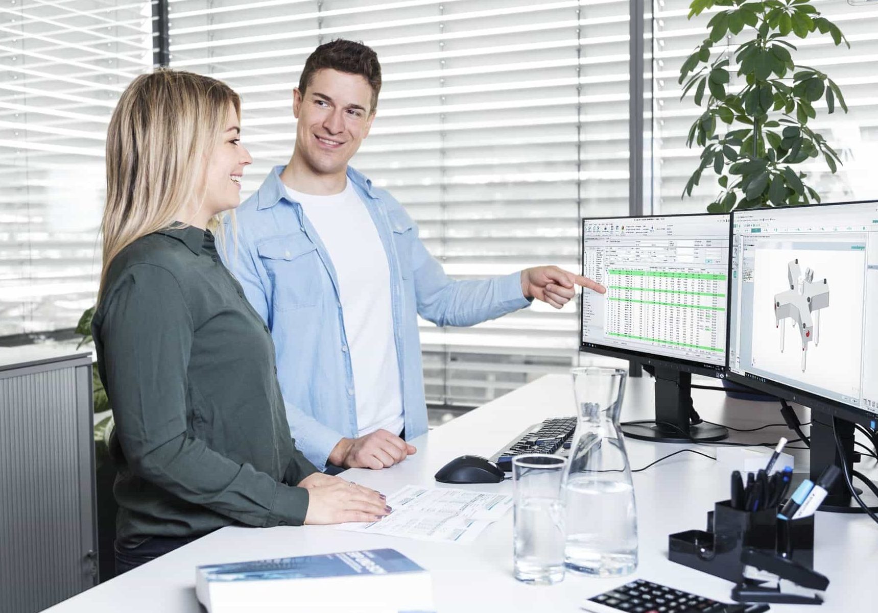 Zwei Kollegen lächeln und besprechen Daten auf Computerbildschirmen im Büro.
